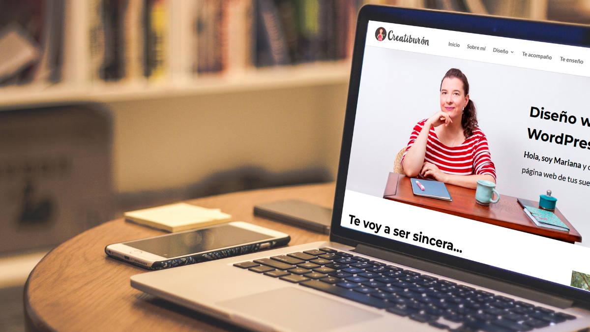 Estrategia web En una mesa se encuentra un ordenador portátil con la pantalla abierta y encendida mostrando la pagina web de Creatiburon donde pretende hablar de Estrategia web